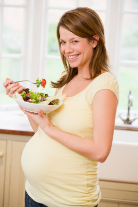 Pregnant woman in kitchen eating a salad smiling